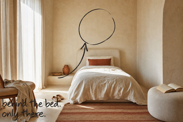 A small guest room in warm plaster, a single bed with an upholstered headboard, the wall behind the headboard circled in open black marker, an arrow from the handwritten words behind the bed, only there, by Willem van der Krieken