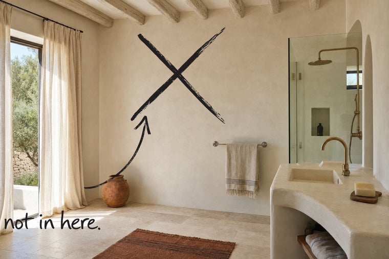 A bathroom in warm off-white tadelakt plaster with a walk-in shower and a moulded plaster washstand, the bare wall struck through with a black marker cross, an arrow from the handwritten words not in here, by Willem van der Krieken