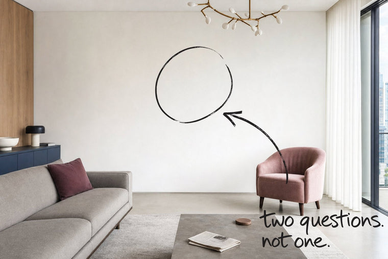 A bright apartment living room with a slate blue sideboard and a dusty pink chair, the empty wall circled in open black marker, an arrow from the handwritten words two questions, not one, by Willem van der Krieken
