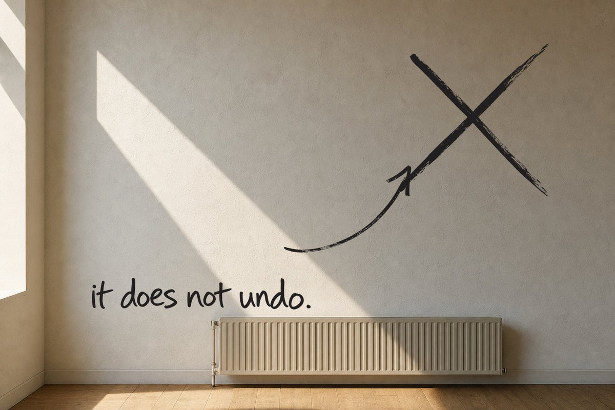 A plaster wall with a hard band of sunlight across it and a radiator below, the sunlit wall struck through with a black marker cross, an arrow from the handwritten words it does not undo, by Willem van der Krieken