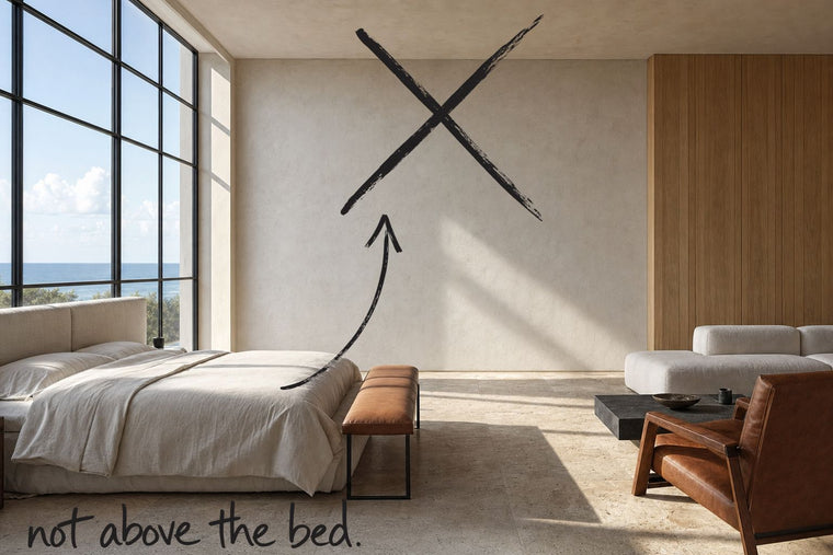 A coastal loft bedroom with a steel-framed window and a travertine floor, the wall above the headboard struck through with a black marker cross, an arrow from the handwritten words not above the bed, by Willem van der Krieken