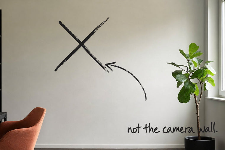 A small home study with a black desk and shelving, a rust-orange chair pulled out, the wall the desk camera frames struck through with a black marker cross, an arrow from the handwritten words not the camera wall, by Willem van der Krieken