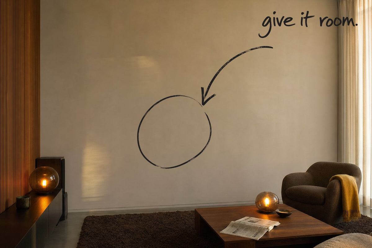 A lived-in living room with a walnut slatted wall and a deep brown rug, amber globe lamps lit low, the empty wall circled in open black marker, a marker arrow running to it from the handwritten words give it room, by Willem van der Krieken