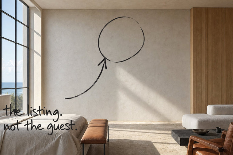 A coastal loft bedroom with a steel-framed window and a travertine floor, the empty wall circled in open black marker, an arrow from the handwritten words the listing, not the guest, by Willem van der Krieken