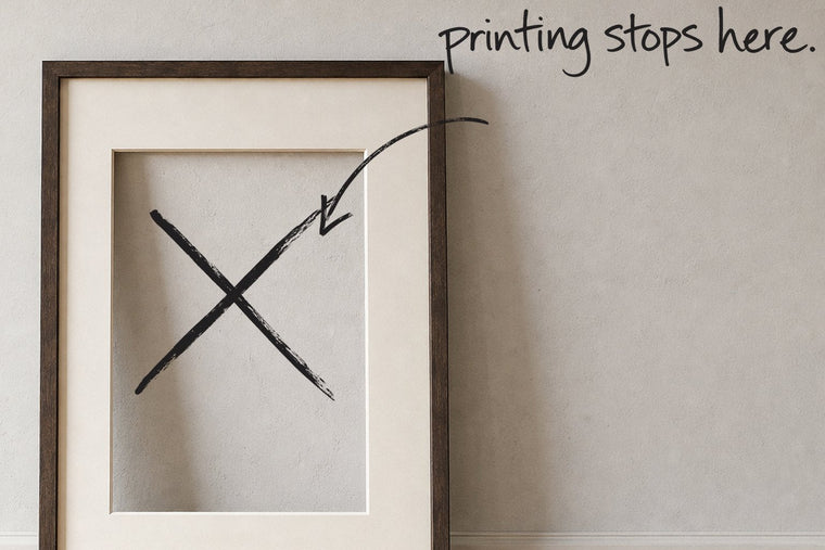 A slim dark frame with a wide paper mount, the opening empty and the wall showing through, the empty opening in the mount struck through with a black marker cross, an arrow from the handwritten words printing stops here, by Willem van der Krieken