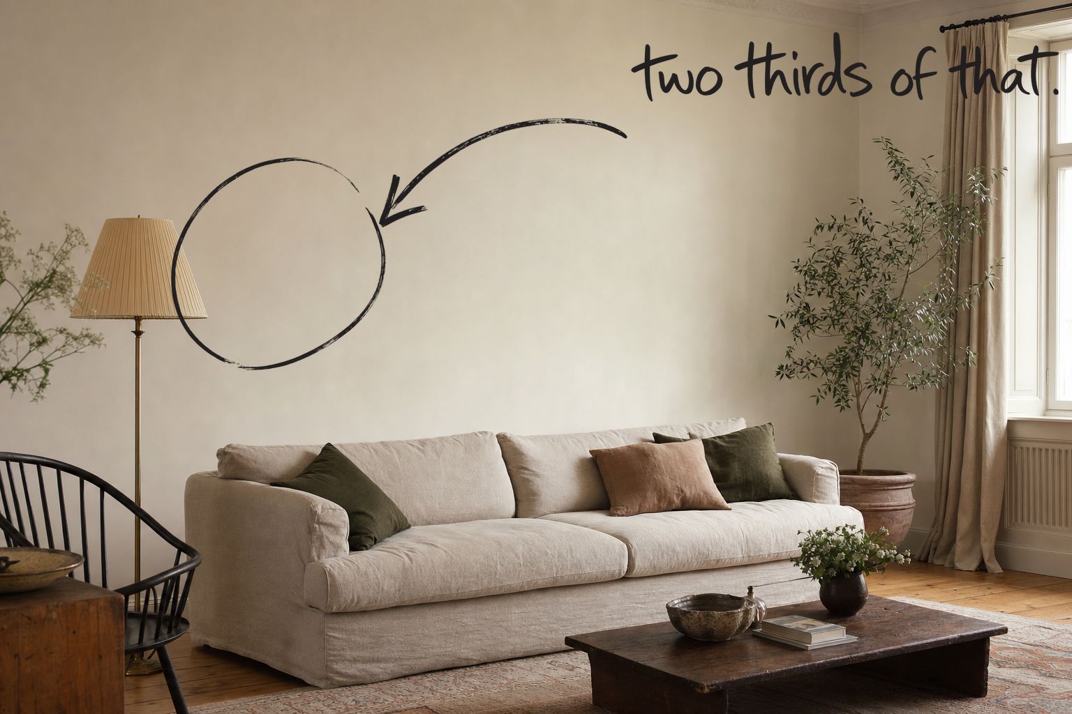 A lived-in living room with a long linen sofa and a completely bare plaster wall above it, the wall above the sofa circled in open black marker, a marker arrow running to it from the handwritten words two thirds of that, by Willem van der Krieken