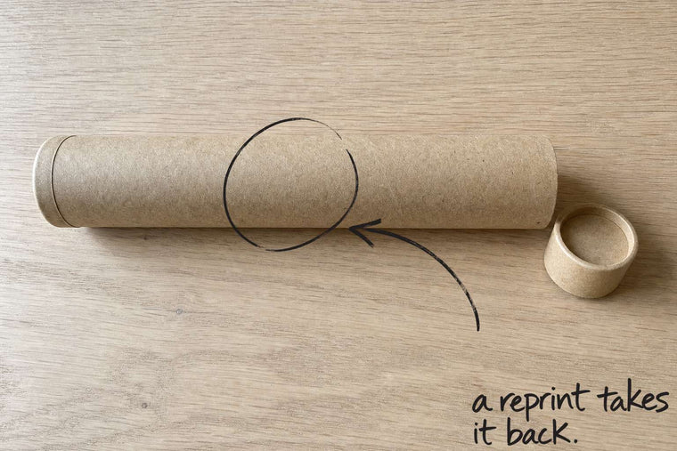 A plain cardboard postal tube lying on an oak tabletop, the postal tube circled in open black marker, an arrow from the handwritten words a reprint takes it back, by Willem van der Krieken